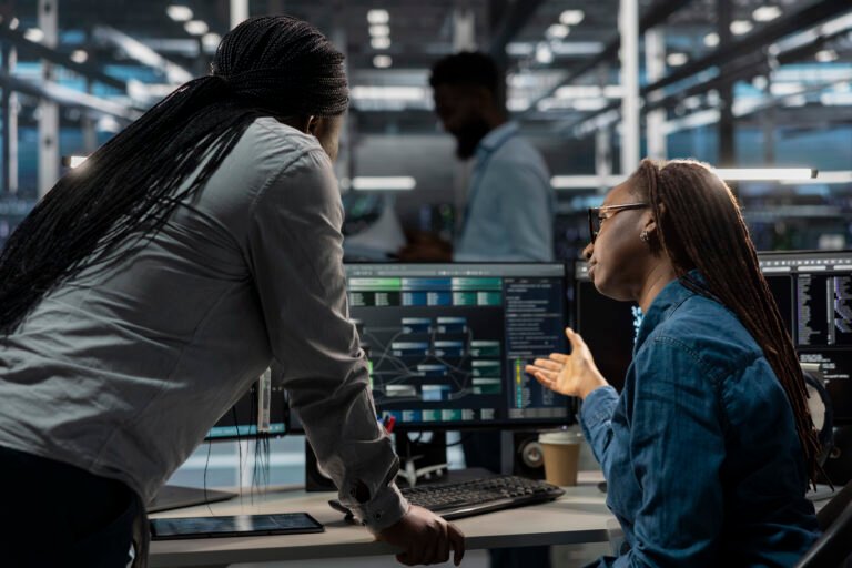 Data center software developers using PC to visualize artificial intelligence neural networks. Server room team leader and worker looking at computer monitor, working together to oversee AI systems